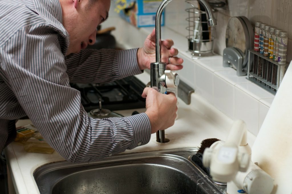 Un homme en train de réparer le robinet d'un évier
